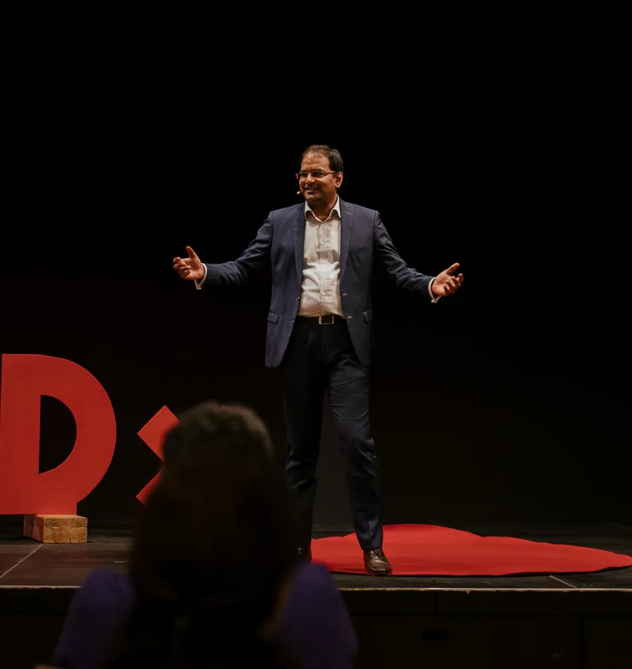 Mithun A. Sridharan on stage at TEDxParadeplatz, arms open, speaking to the audience