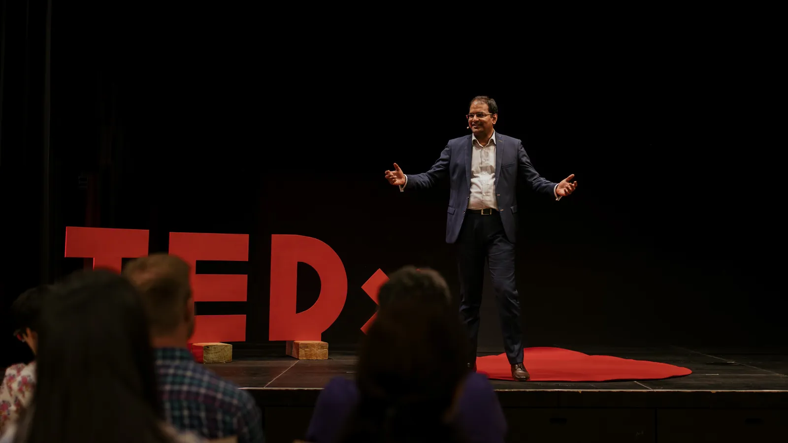 Mithun A. Sridharan on stage at TEDxParadeplatz, arms open, speaking to the audience